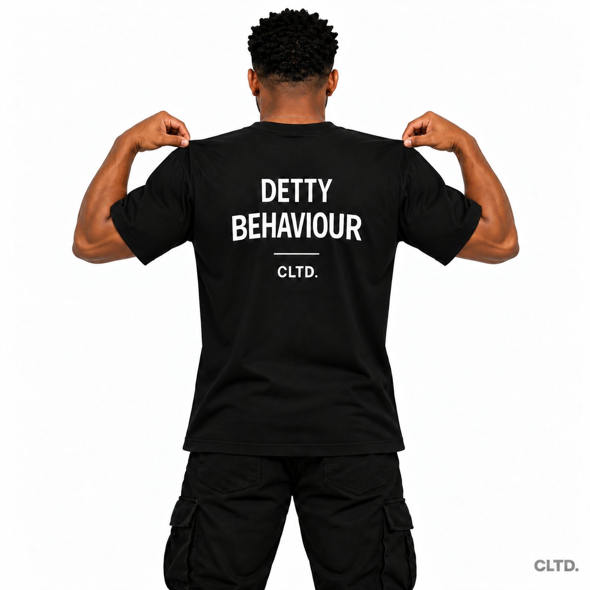 Detty Behaviour black T-shirt — male model holding shirt at shoulders to show back design